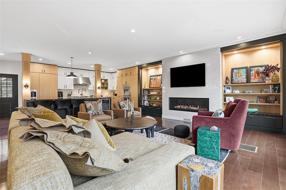 Completed living room at 519 54th Street, with a lit fireplace, illuminated shelving, and an open kitchen with wood cabinetry